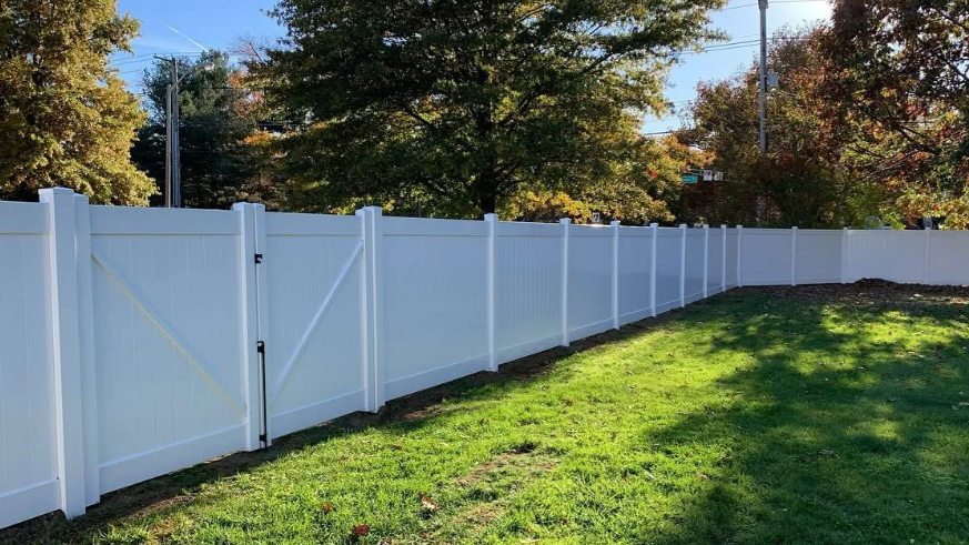 White vinyl fence beside a green grassy yard with trees in the background