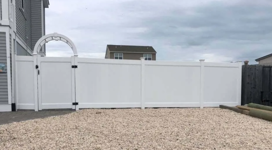 White vinyl backyard fence with gate and gravel yard under cloudy sky