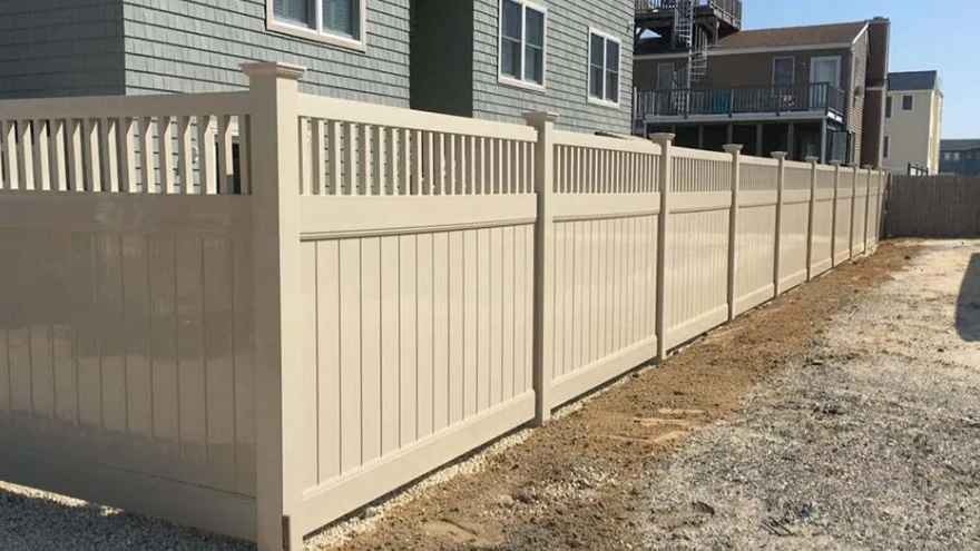 Beige vinyl privacy fence along a gravel side yard beside houses on a sunny day