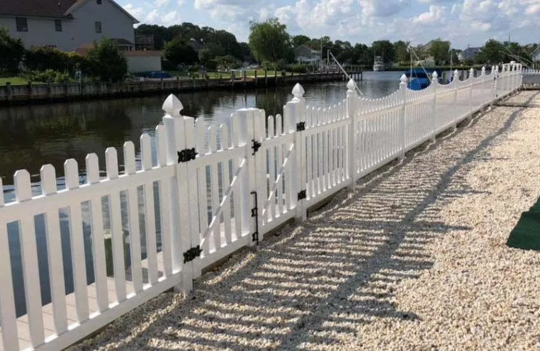 White picket fence along a canal beside a gravel path, with houses in the background