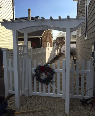White pergola over a picket gate with a holiday wreath in a narrow side yard