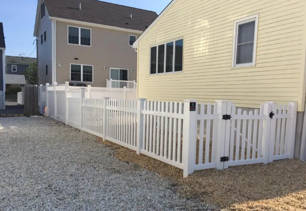 White vinyl fence beside yellow and beige houses on a gravel yard