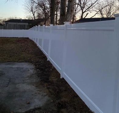 White vinyl privacy fence along a backyard edge beside a concrete path at dusk.
