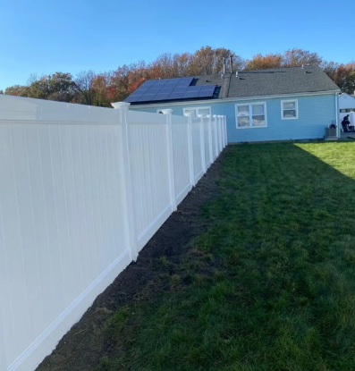 White vinyl fence beside a green lawn, leading toward a light blue house with solar panels.