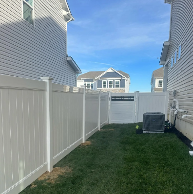 Narrow grass backyard between white vinyl fences and gray houses under a blue sky