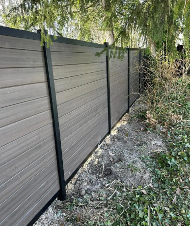 Gray and black fence panels beside a weedy path under hanging tree branches