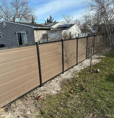 Tan privacy fence with black posts along a grassy yard beside a house and trees