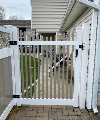 White gate beside a driveway under a covered patio, with a stroller behind the slats