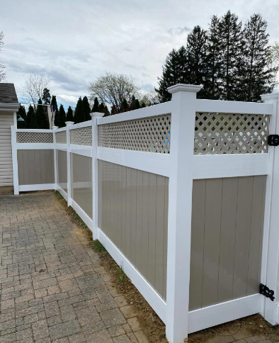 White lattice fence with taupe panels along a paved driveway outdoors