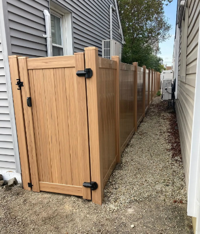 Wooden gate and privacy fence along a narrow gravel side yard beside a gray house
