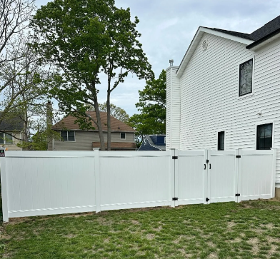 White vinyl fence beside a white house in a grassy backyard, with trees and neighboring homes beyond.