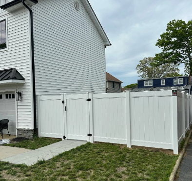 White vinyl privacy fence beside a white house in a grassy yard, with neighboring homes in the background