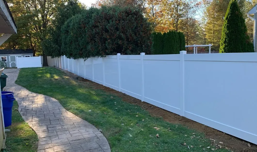 Curved brick path beside a white vinyl fence and green lawn in a suburban yard