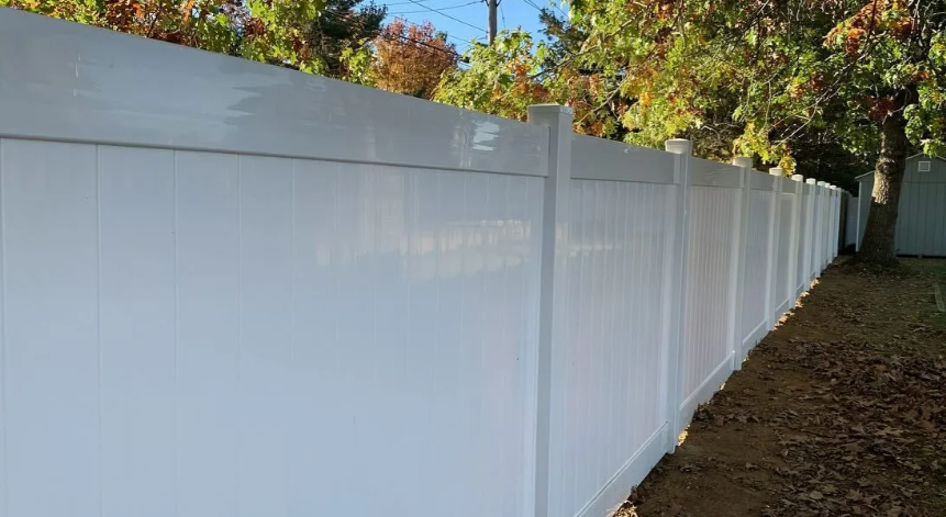 Long white vinyl fence along a grassy yard with autumn trees in the background