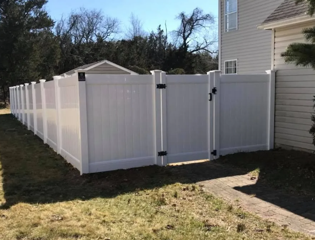 White vinyl privacy fence with a gate beside a beige house in a grassy yard