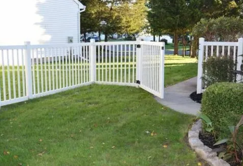 White vinyl fence and gate beside a lawn, with a curved stone path and trimmed hedges in a yard.