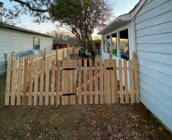 Wooden gate across a backyard entrance beside a white house, with a tree and garage in the background