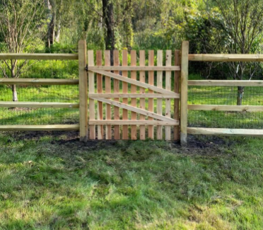 Wooden garden gate with diagonal bracing between split-rail fences in a grassy yard