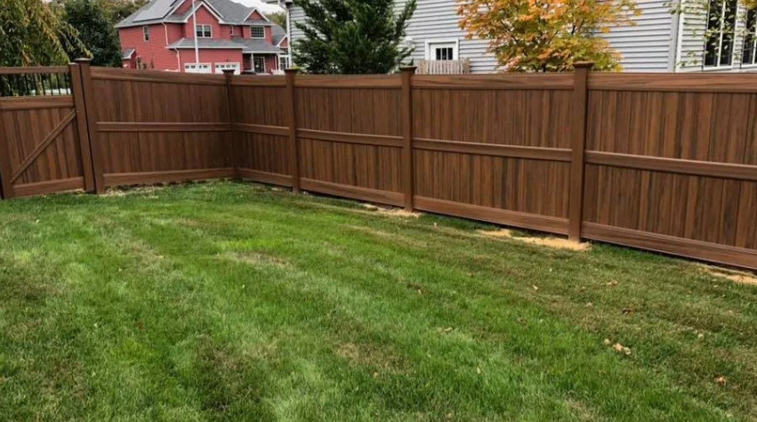 Grassy backyard enclosed by a brown wooden fence, with a red house visible beyond it.