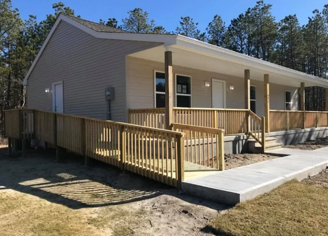 Single-story house with a wraparound wooden ramp and porch railing on a sunny day