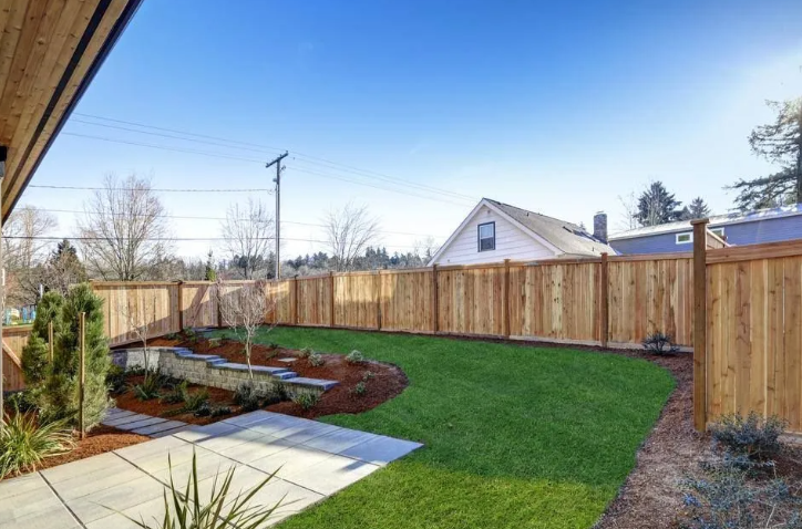 Backyard with green lawn, raised garden beds, and a wooden fence under a blue sky