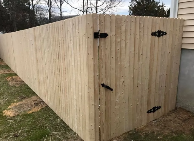 Tan wooden privacy fence corner with black hinges and latch on a grassy yard