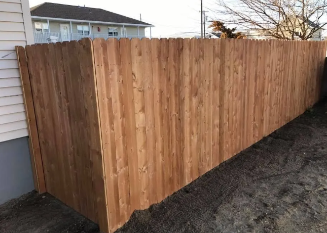 New wooden privacy fence beside a house on a dirt lot