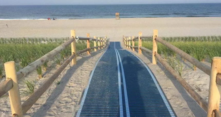 Wooden boardwalk through dunes to a sandy beach and ocean under a clear sky