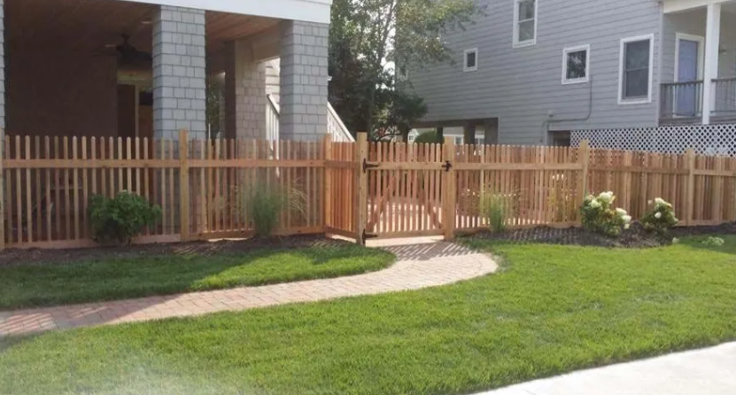Wooden fence enclosing a small green lawn beside a house with a curved sidewalk.