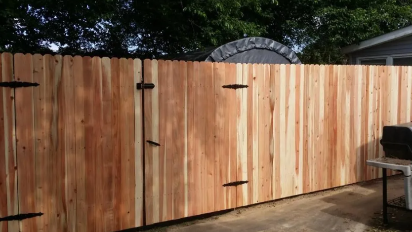 Wooden backyard fence with vertical planks and black hinges, set beside a patio grill.