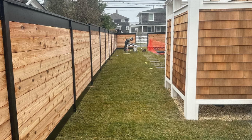 Narrow grassy side yard between wooden fences and a house with shingled siding, leading to a gate.