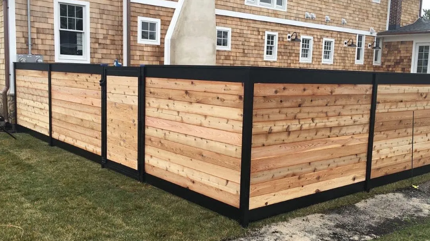 Black-framed wooden privacy fence enclosing a corner yard beside a brick house