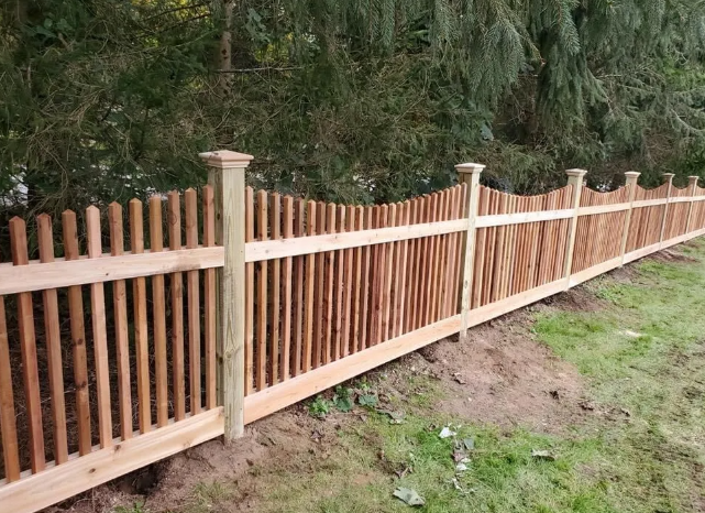 Wooden fence with beige posts along a grassy path beside dense green vegetation