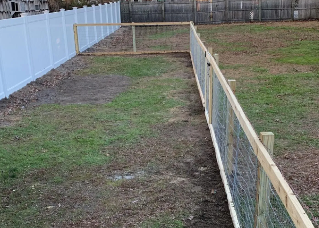 Backyard fenced dog run with wire mesh and a white privacy fence, mostly bare ground and grass