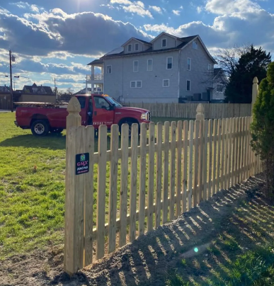 Red pickup truck behind a tan picket fence in a sunny residential yard