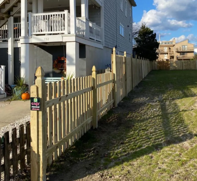 Wooden fence beside a gray house and grassy alley under a bright sky