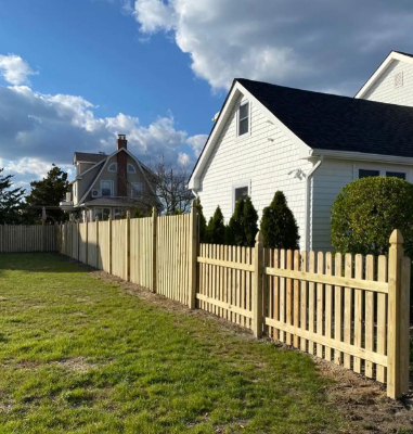 Wooden fence beside white houses and green lawn under a blue sky with clouds