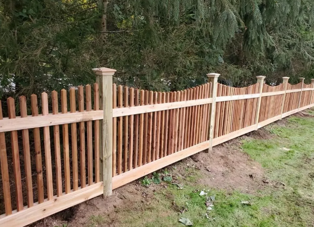 Wooden fence with tan posts and dark slats along a grassy, wooded edge