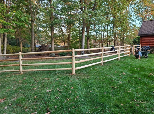 Wooden fence along a grassy yard with trees in the background and a house on the right.