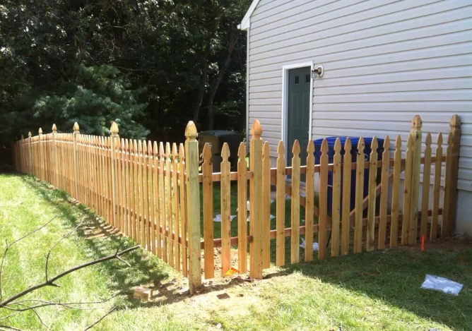 Wooden picket fence along a grassy yard beside a white house with a green door
