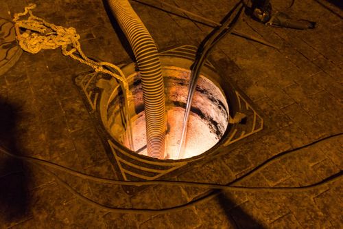 Orange-lit industrial shaft with a hose and cables descending into a circular opening