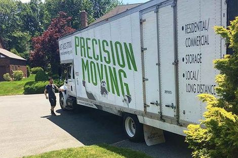 A precision moving truck is parked in a driveway next to a house.