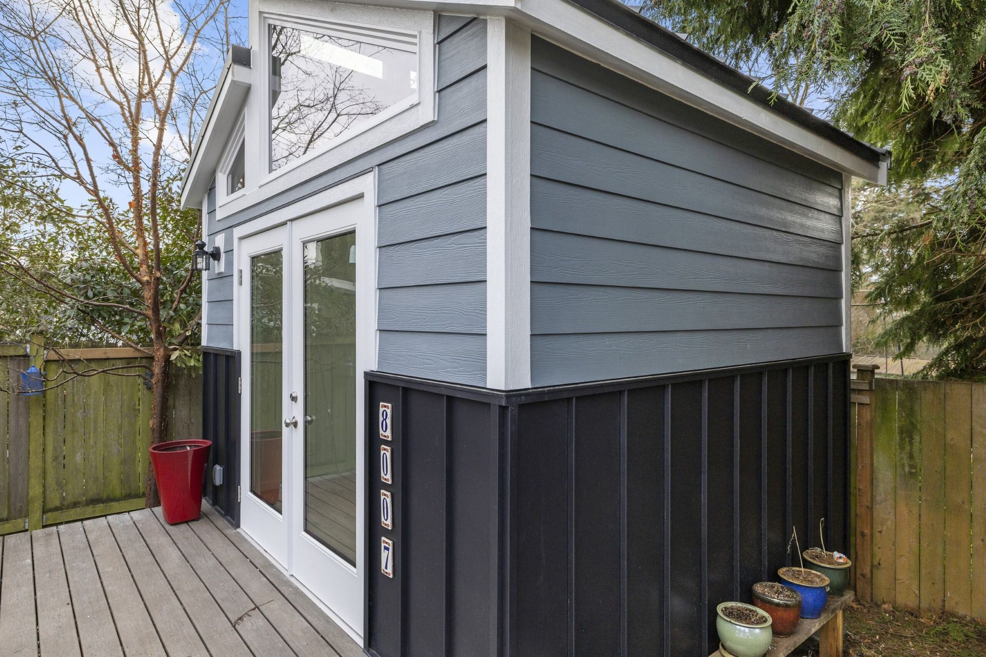 A small shed with a deck and potted plants in front of it.