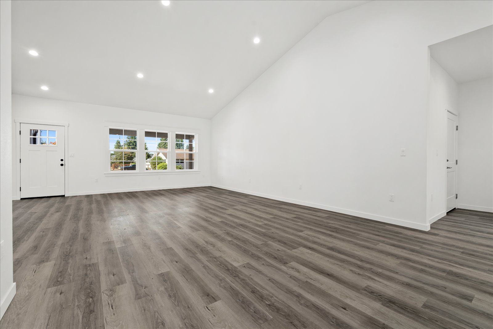 An empty living room with hardwood floors and white walls.