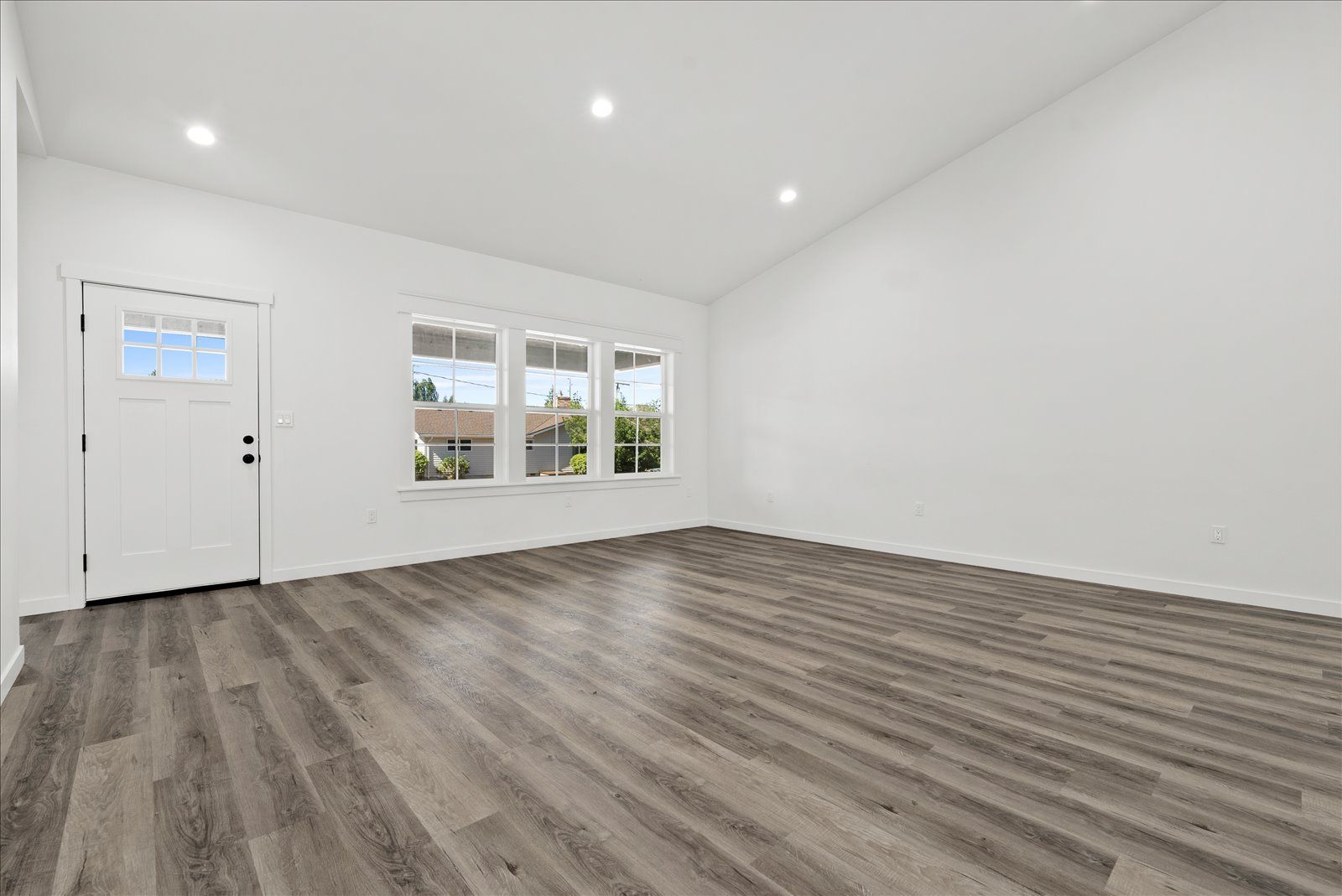 An empty living room with hardwood floors and white walls.