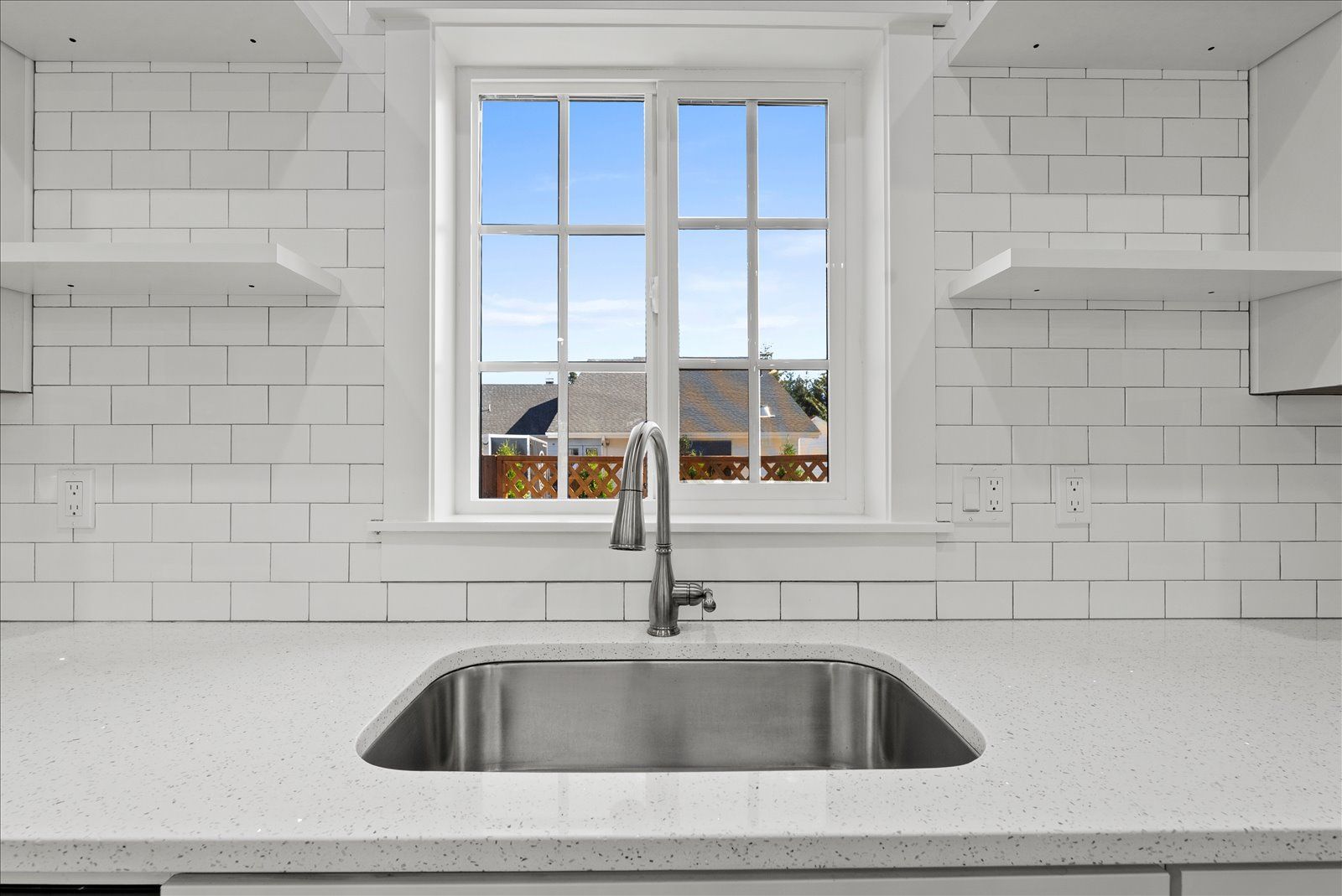 A kitchen sink in front of a window with a view of a house.