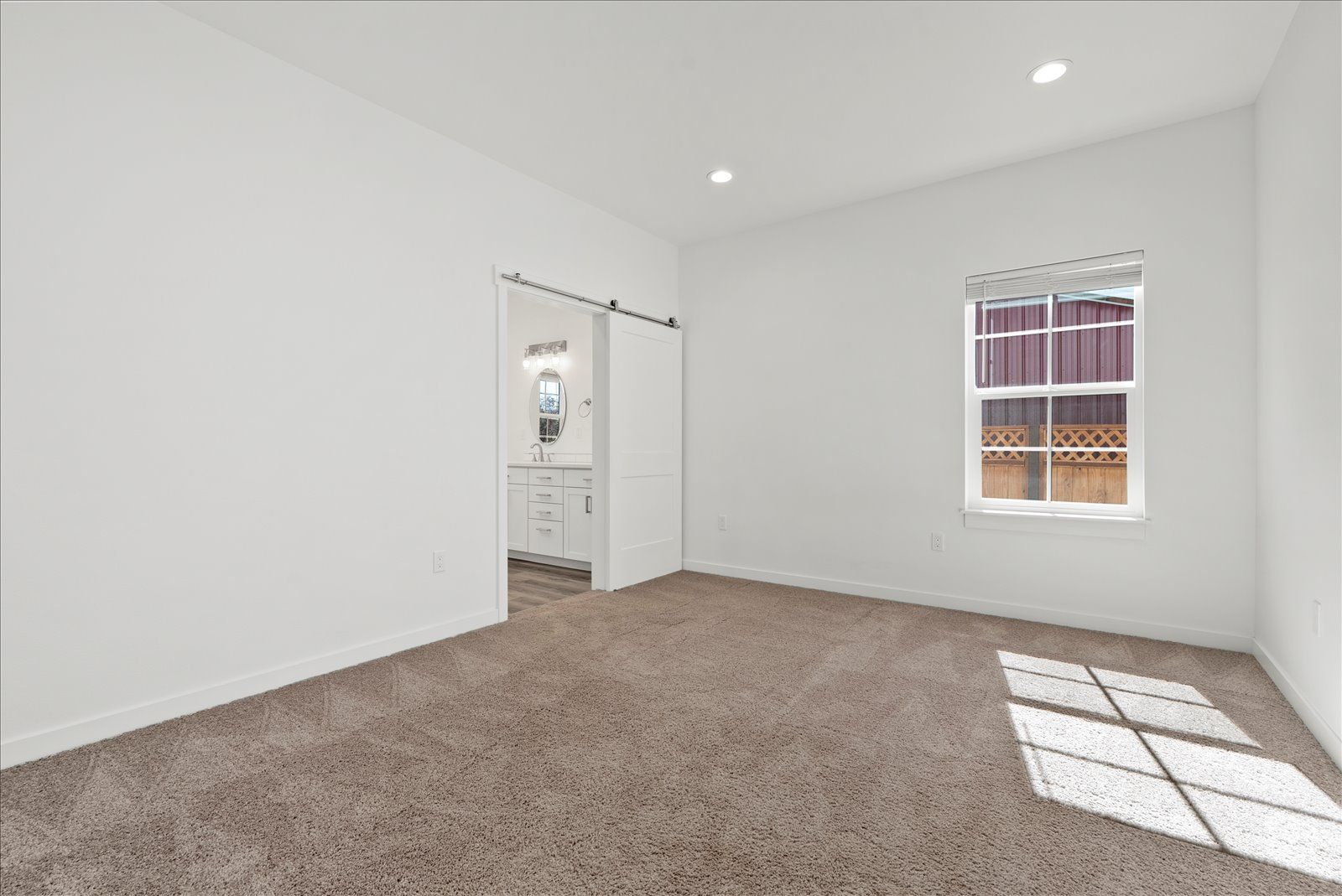 An empty bedroom with a sliding barn door and a window.