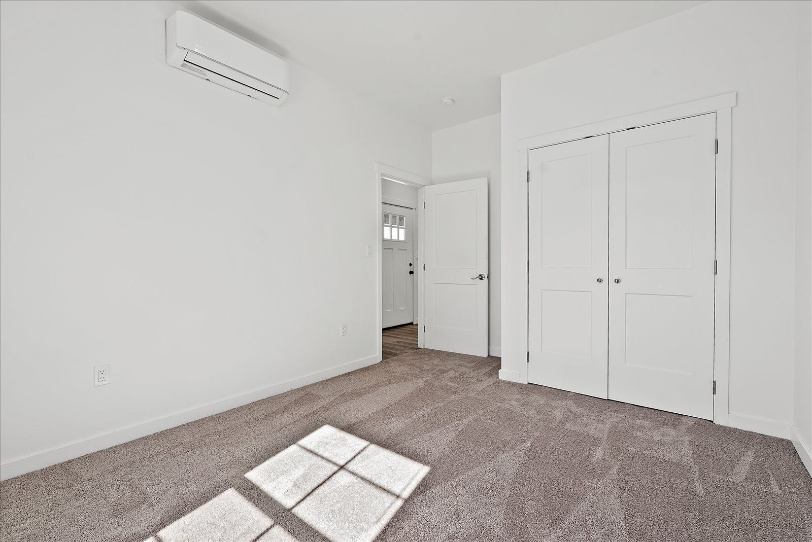 An empty bedroom with a carpeted floor , white walls , and a window.