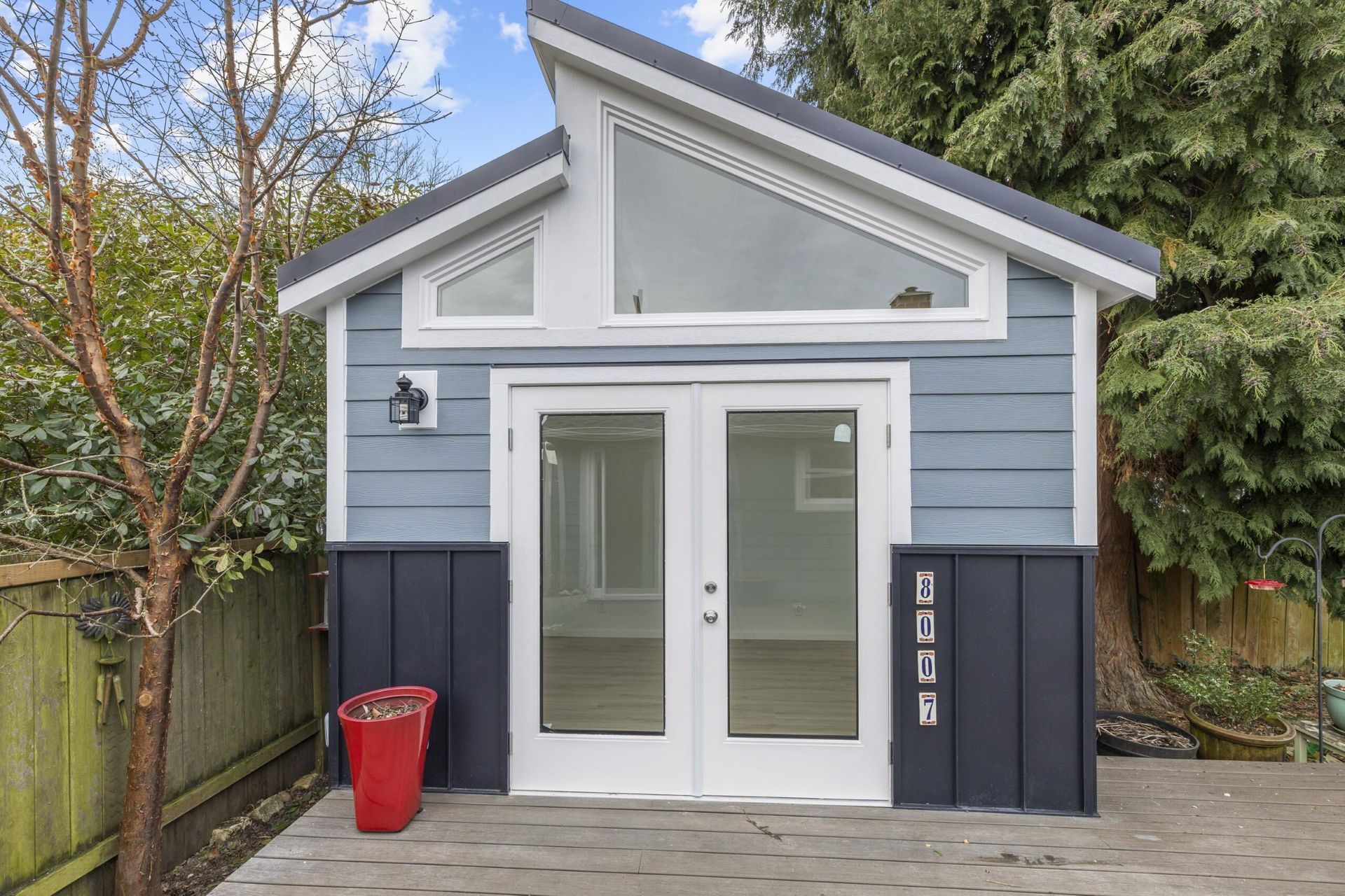 A blue and white shed with a red trash can in front of it