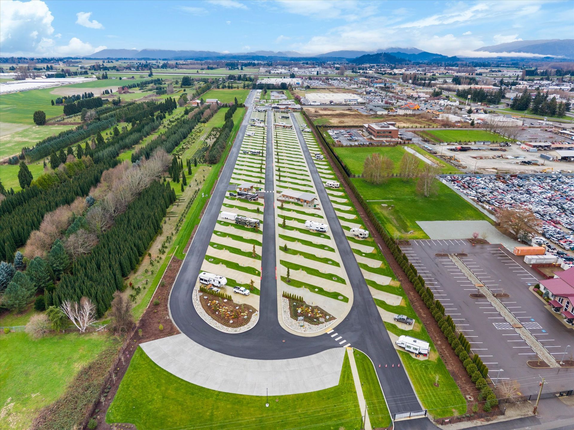 Aerial view of an RV park featuring organized parking rows, green grass strips, and nearby trees next to a paved lot.